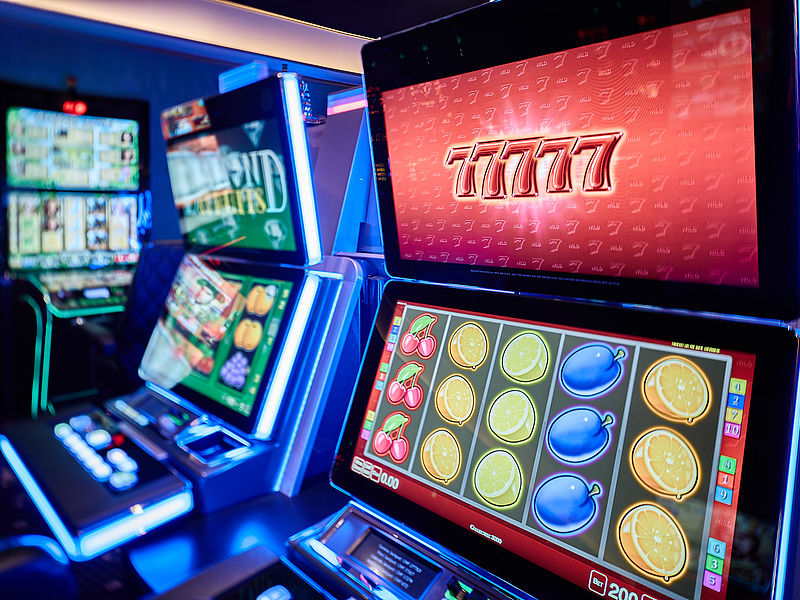 Beleuchtete Reihe von bunten Spielautomaten im Casino Bad Ragaz; der Hauptbildschirm zeigt Fruchtsymbole und gewinnende Siebener. Das lebendige Ambiente suggeriert Spannung und Glück.