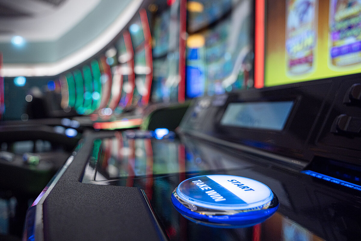 Nahaufnahme eines eleganten Casino-Spielautomaten mit bunten Bildschirmen im Hintergrund. Die Kulisse vermittelt Spannung und Vorfreude.