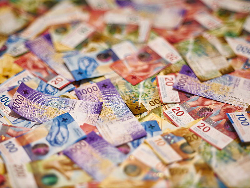  Eine bunte Auswahl an Schweizer Franken-Banknoten, zufällig verstreut. Die Banknoten weisen unterschiedliche Nennwerte und lebendige Designs auf und vermitteln Reichtum und Vielfalt.