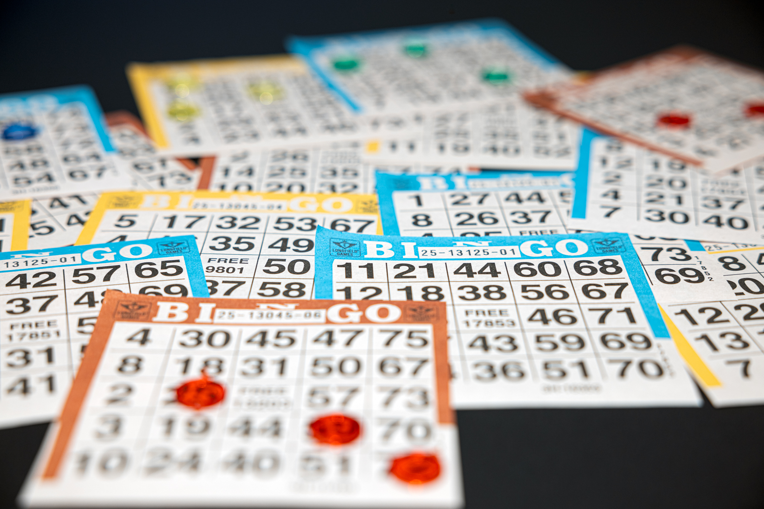 Ein verstreuter Stapel bunter Bingokarten mit verschiedenen Zahlen. Einige Karten haben rote Spielsteine. Die Szene suggeriert ein laufendes Bingospiel.